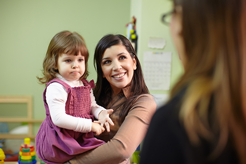 woman smiling and holding toddler while talking with another woman